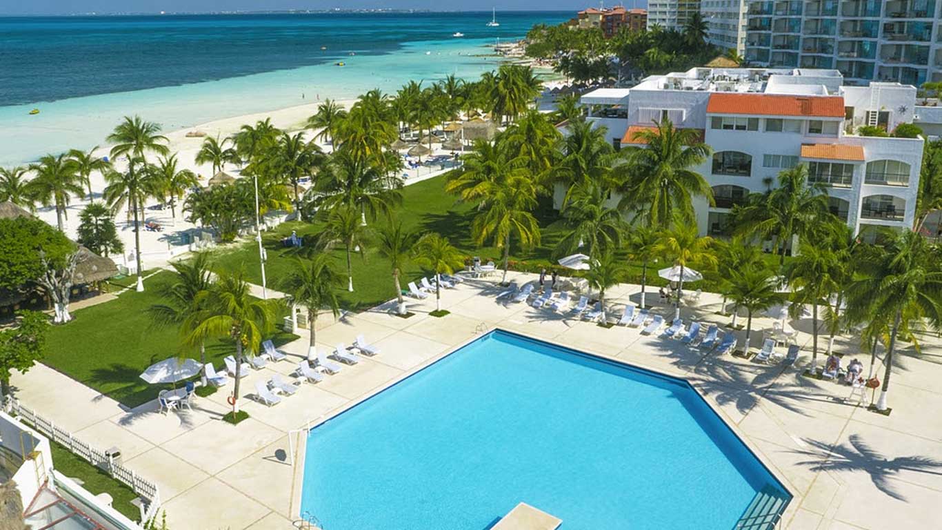 Una alberca frente al mar, con el hotel rodeado de amplias áreas verdes, palmeras y cómodos camastros para relajarse.
