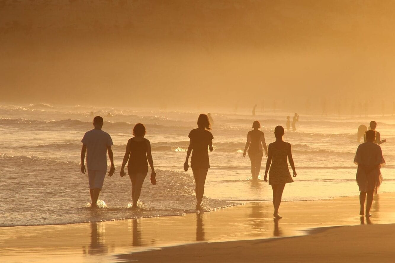 Grupo de amigos caminando por la orilla de una playa mexicana, disfrutando del atardecer y paisaje costero en un ambiente relajado y alegre