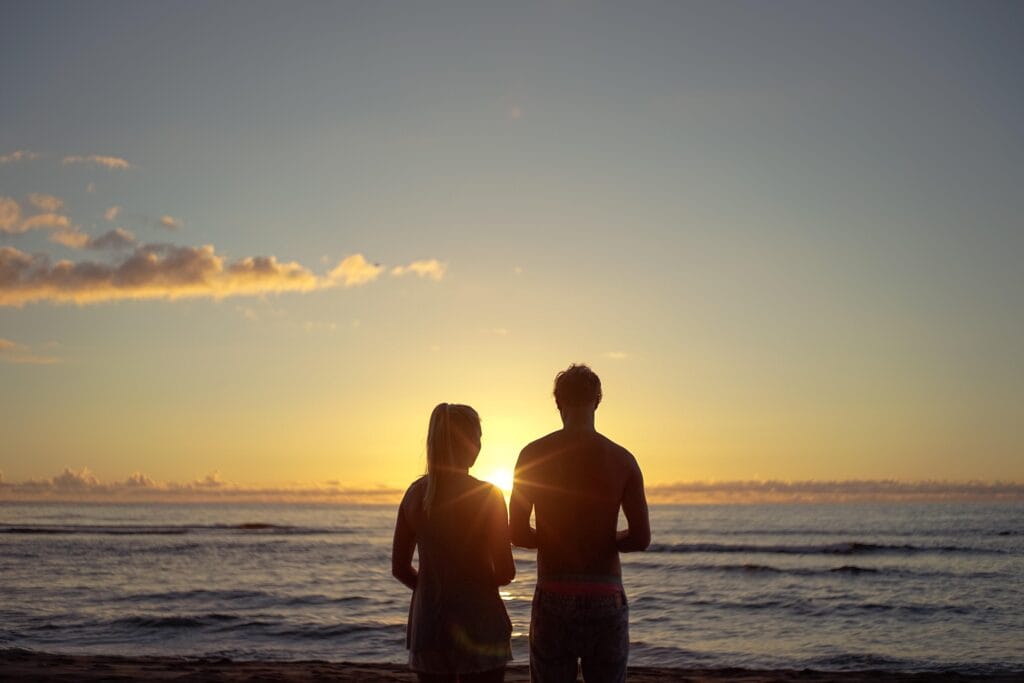 Pareja disfrutando de un hermoso atardecer frente a las olas del mar, una de las actividades más románticas ideales para hacer en pareja durante unas vacaciones junto al mar.