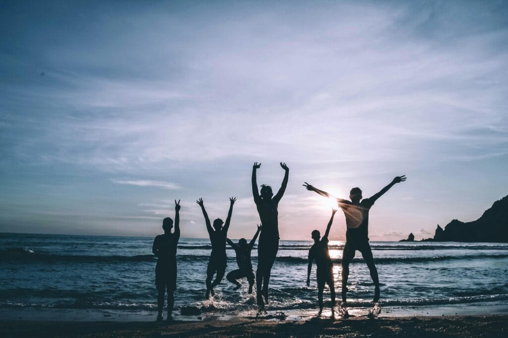 Seis amigos disfrutando mientras saltan y realizan actividades divertidas en la playa con amigos durante un día soleado.